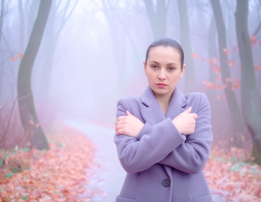 Femme aux bras croisés et au regard froid dans une forêt d’hiver brumeuse