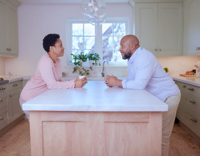 Couple debout dans une cuisine moderne, en pleine discussion calme autour d’un îlot